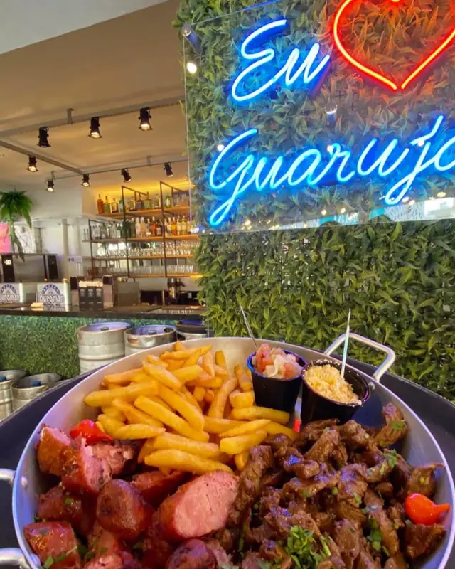 Porção de batata frita e carnes, com um letreiro de neon ao fundo